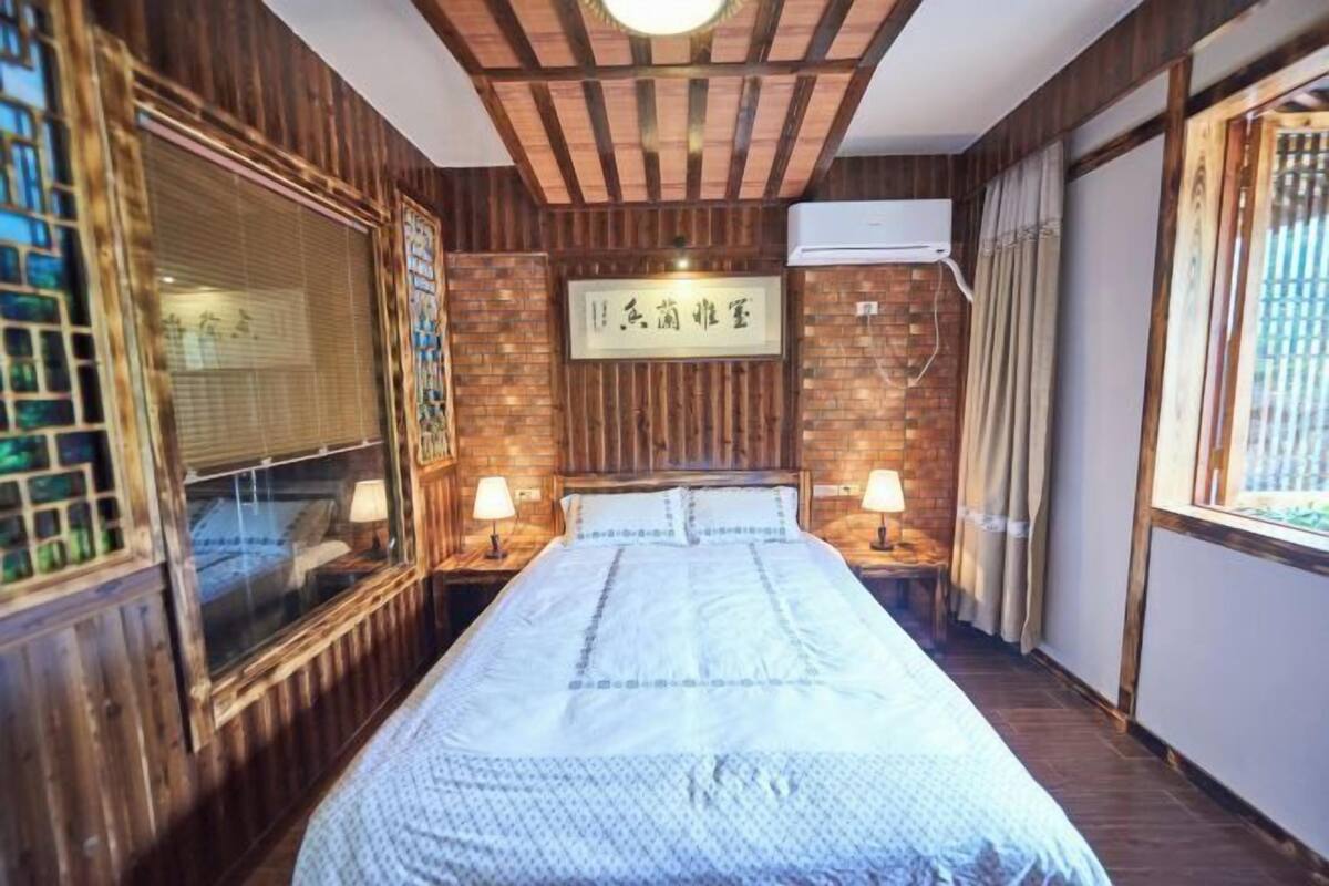 A room with a wooden paneled wall, a bed with a white bedspread, two bedside lamps, and an air conditioning unit.