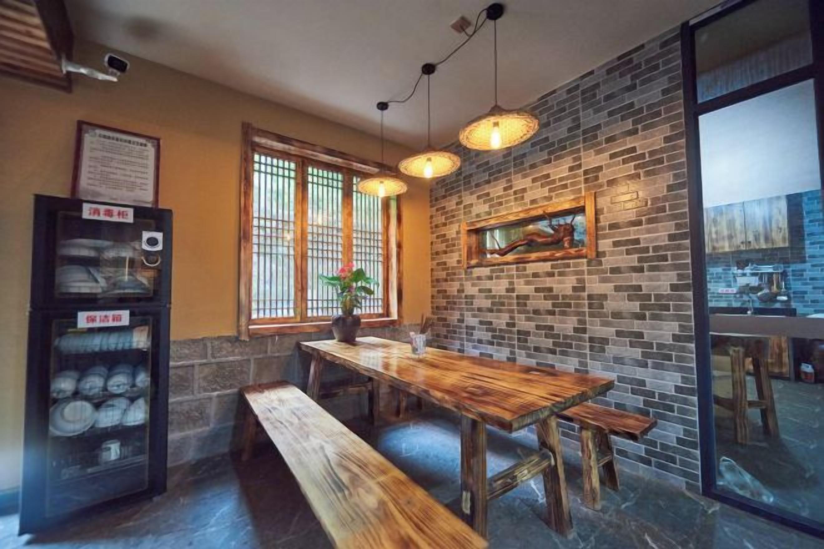A restaurant interior with a brick wall, wooden table, benches, hanging lights, and a vending machine.