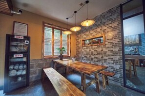 L’intérieur d’un restaurant avec un mur en briques, une table en bois, des bancs, des luminaires suspendus et un distributeur automatique.