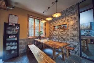 Interior de restaurante con pared de ladrillo, mesa de madera, bancos, luces colgantes y una máquina expendedora.