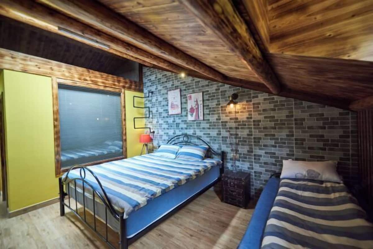 A room with a bed, a window, a brick wall, and a wooden ceiling.