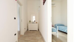 A narrow hallway with a white dresser, a bed with a blue bedspread, and a white chair. - Villetta del Chidro by BarbarHouse (San Pietro in Bevagna)