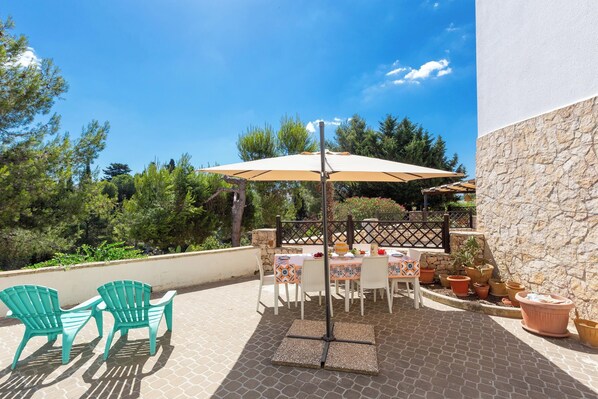 An outdoor patio with a table and chairs, surrounded by potted plants and a stone wall.