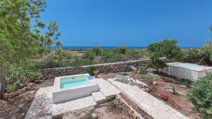Ein Poolbereich mit einer Steinmauer, einem kleinen Pool und Blick aufs Meer.