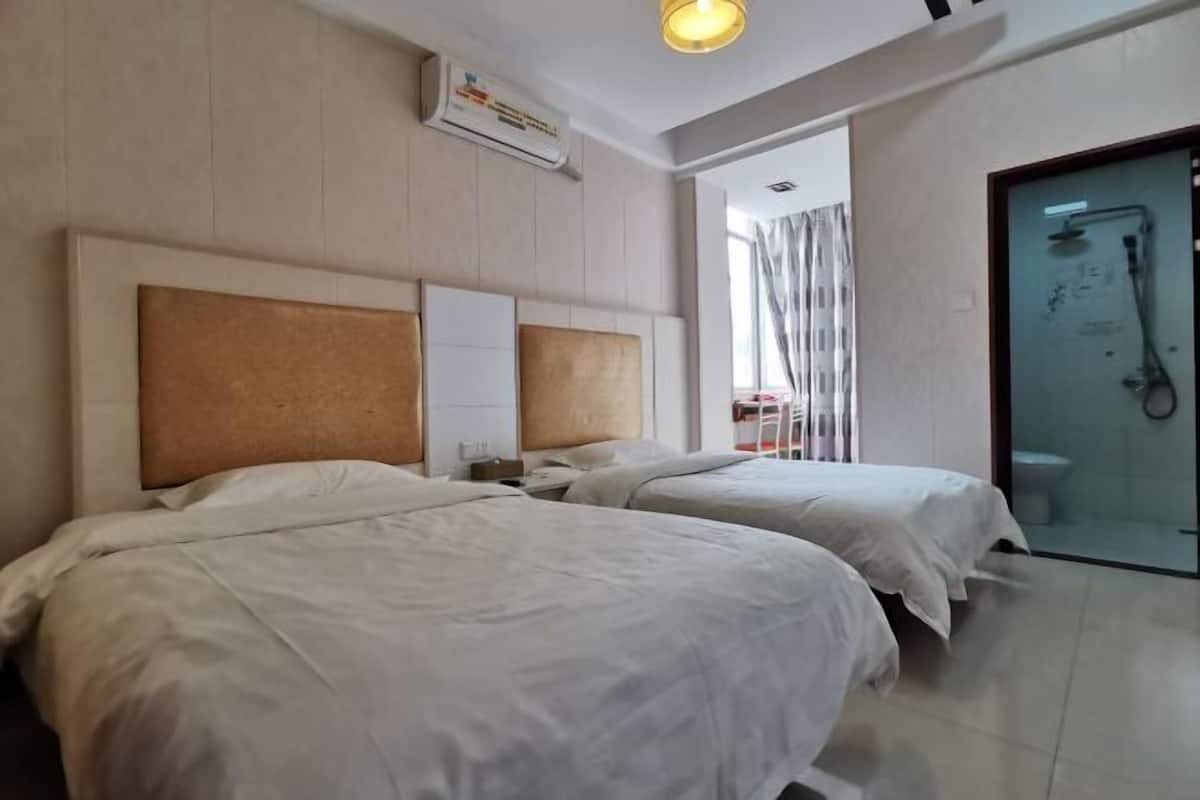 A hotel room with two beds, a shower area, and a visible bathroom.