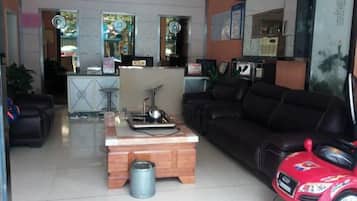 A living room with a black sofa, a wooden coffee table, a red toy car, and a kitchen area in the background.