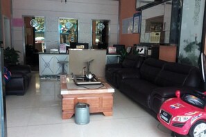 Una sala de estar con un sofá negro, una mesa de centro de madera, un coche de juguete rojo y una cocina al fondo.