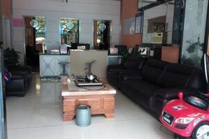 Una sala de estar con un sofá negro, una mesa de centro de madera, un coche de juguete rojo y una cocina al fondo.
