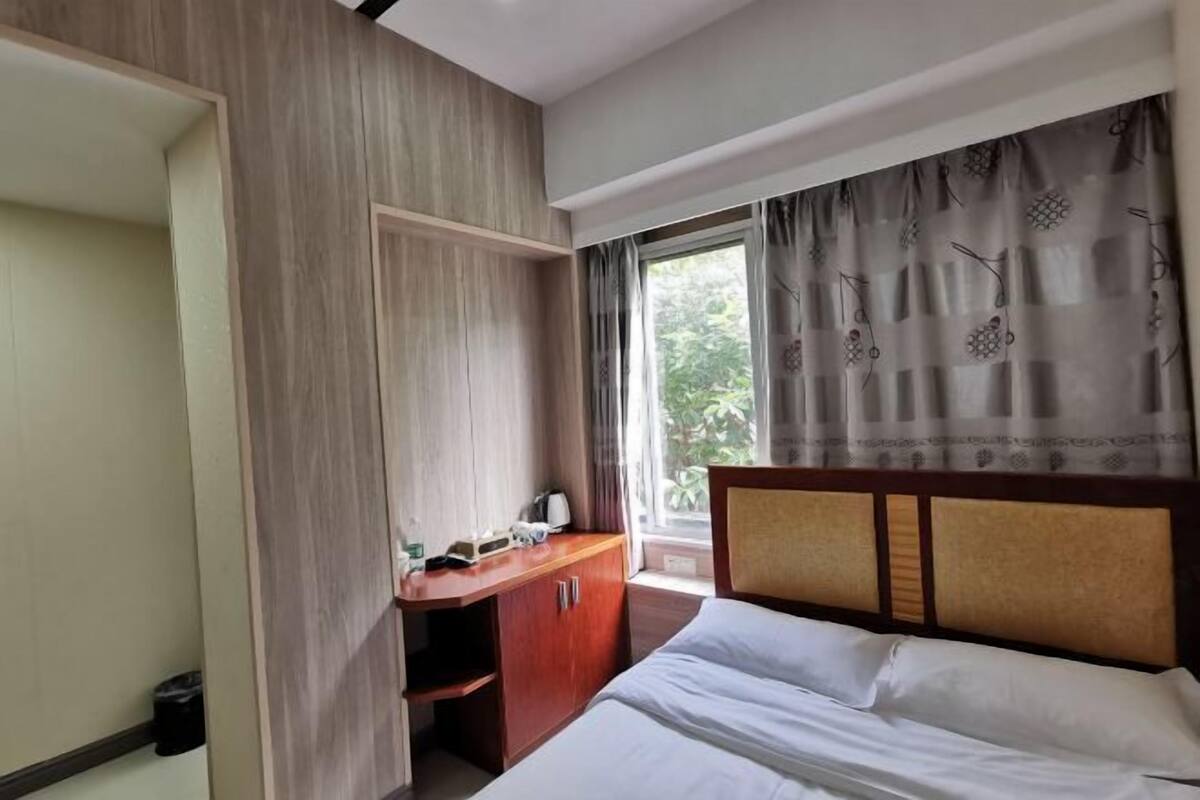 A hotel room with a bed, a wooden desk, and a window with curtains.