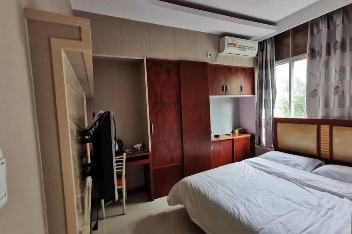 Hotellihuone, jossa on sänky, työpöytä, vaatekaappi ja ikkuna, jossa on verhot.