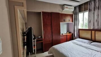 A hotel room with a bed, a desk, a wardrobe, and a window with curtains.
