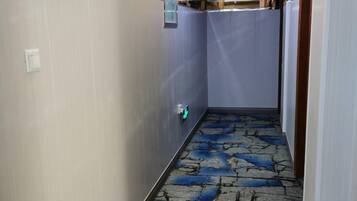 Un estrecho pasillo con alfombra estampada, un interruptor de luz y una puerta a la derecha.