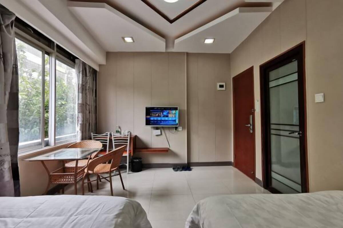 A hotel room with a bed, a TV mounted on the wall, a dining table with chairs, and a window with curtains.