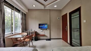 A hotel room with a bed, a TV mounted on the wall, a dining table with chairs, and a window with curtains.
