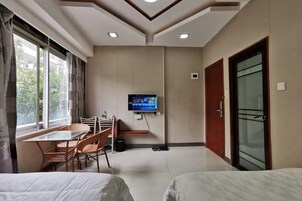 Habitación de hotel con cama, televisor montado en la pared, mesa de comedor con sillas y ventana con cortinas.