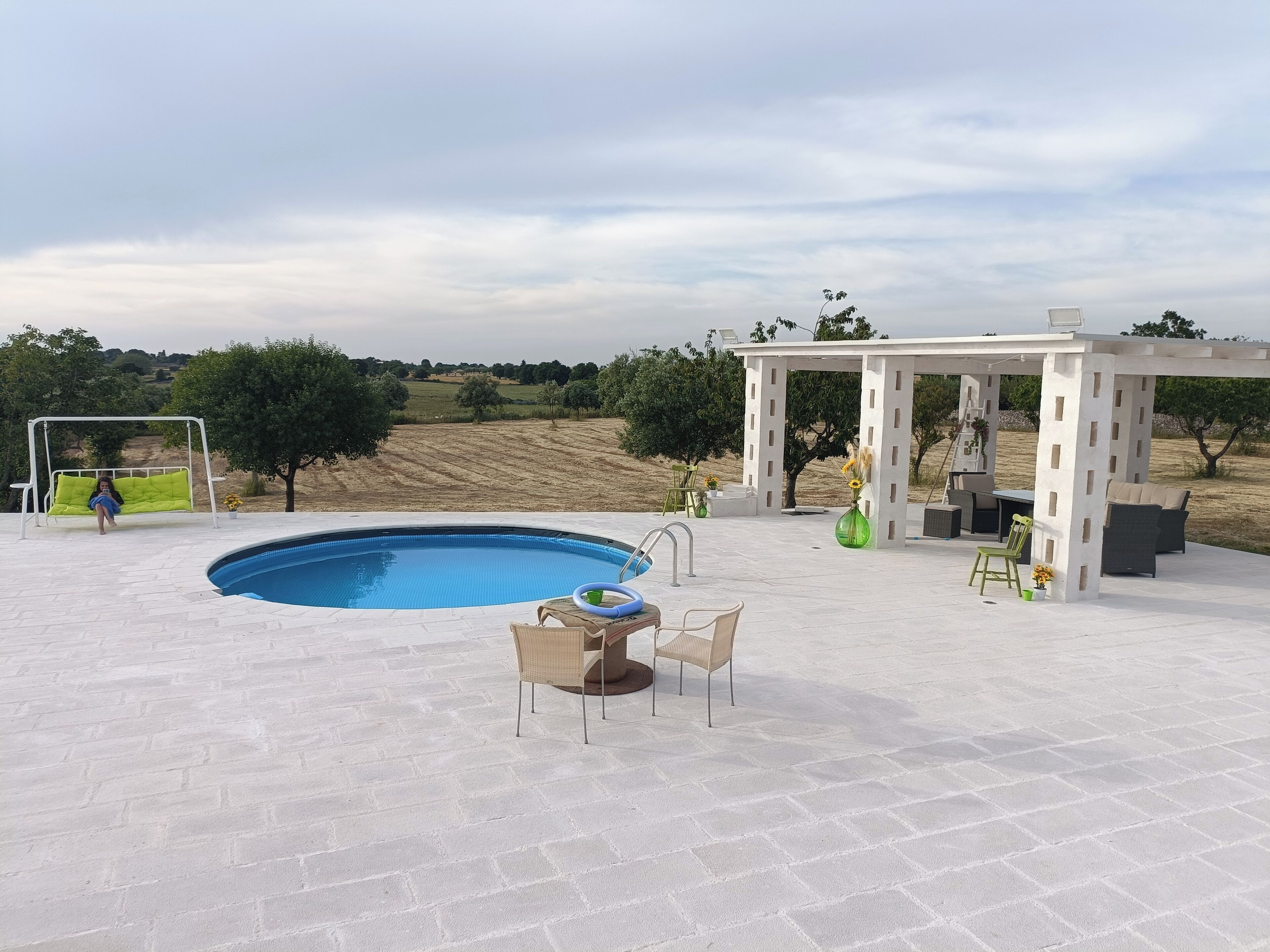 A pool area with a pergola, outdoor seating, and a view of the countryside.