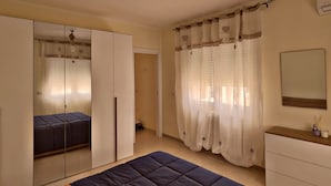 Un dormitorio con cama, armario, espejo y cortinas.