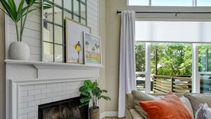 A living room with a fireplace, a sofa, and a large window with a view of trees.