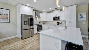 A modern kitchen with white cabinets, stainless steel appliances, and pendant lighting.