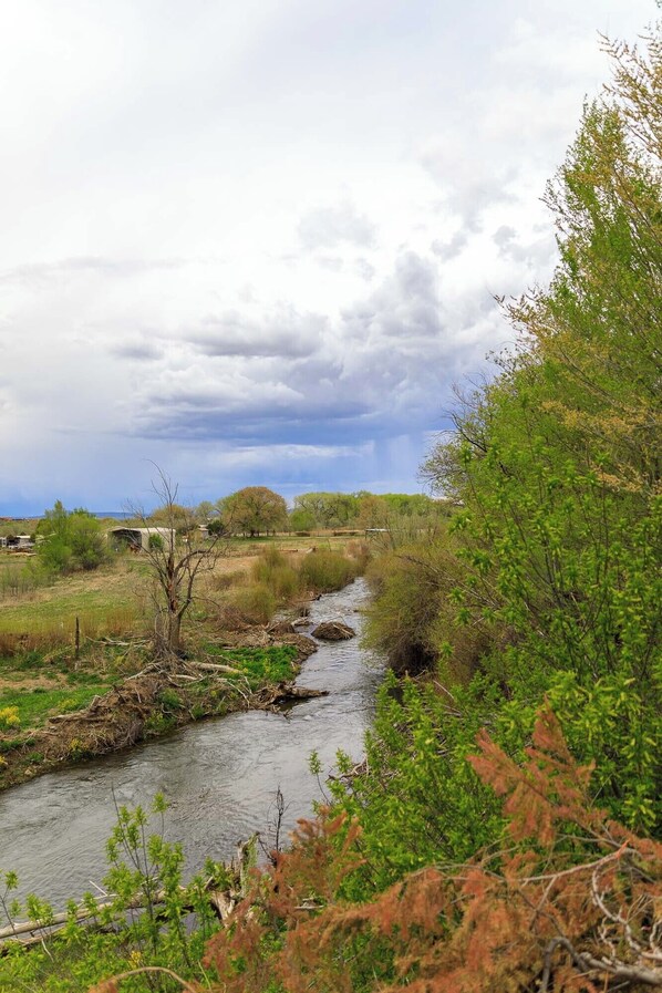 A river flowing through a natural landscape with trees and a small structure in the background.