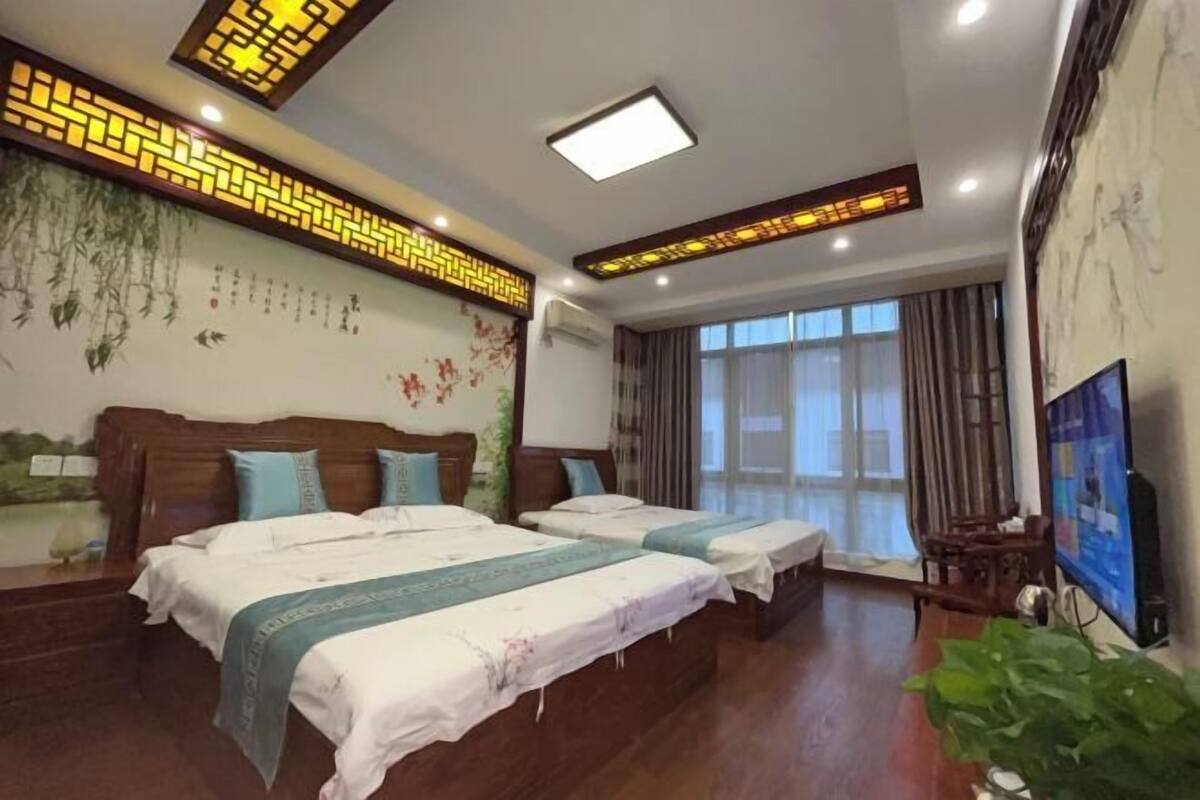 A hotel room with two beds, a TV, a large window, and traditional decor.