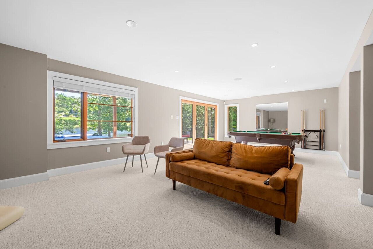 A spacious room with a beige carpet, a brown leather sofa, two armchairs, and a pool table.
