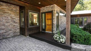 Ein modernes Haus mit Natursteinfassade, Holzbalken und einer überdachten Veranda.