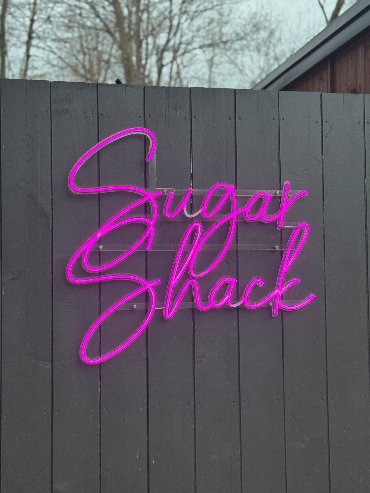 Un cartello luminoso al neon su una staccionata di legno con la scritta 'Sugar Shack'.