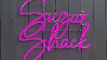 Un cartello luminoso al neon su una staccionata di legno con la scritta 'Sugar Shack'.