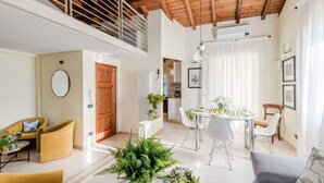 A spacious living area with a high ceiling, a dining table set for four, and a cozy seating area with yellow chairs.