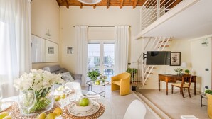 A spacious living area with a dining table set for four, a sofa, a yellow armchair, and a TV mounted on the wall.