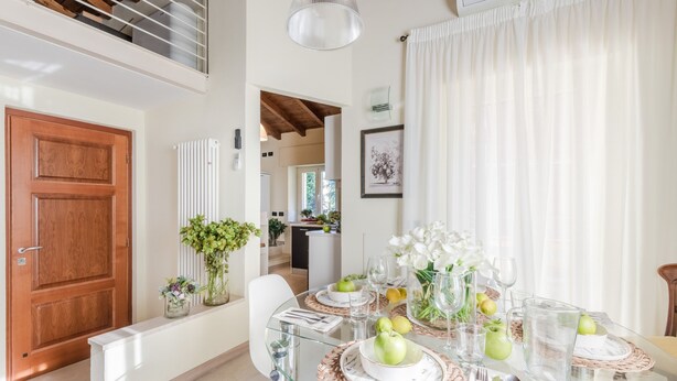 A dining area with a glass table, white chairs, and a wooden door.