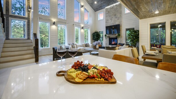 Un comedor amplio con una mesa de mármol, una tabla de madera con quesos y frutas variados, y una zona de estar acogedora con sofás y sillones.