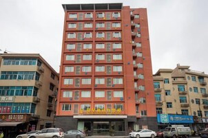 Un hotel a più piani con facciata rossa, numerosi balconi e un ingresso a livello strada con segnaletica.