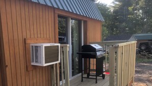 En træhytte med ståltag, grill og en lille terrasse med trapper til døren.