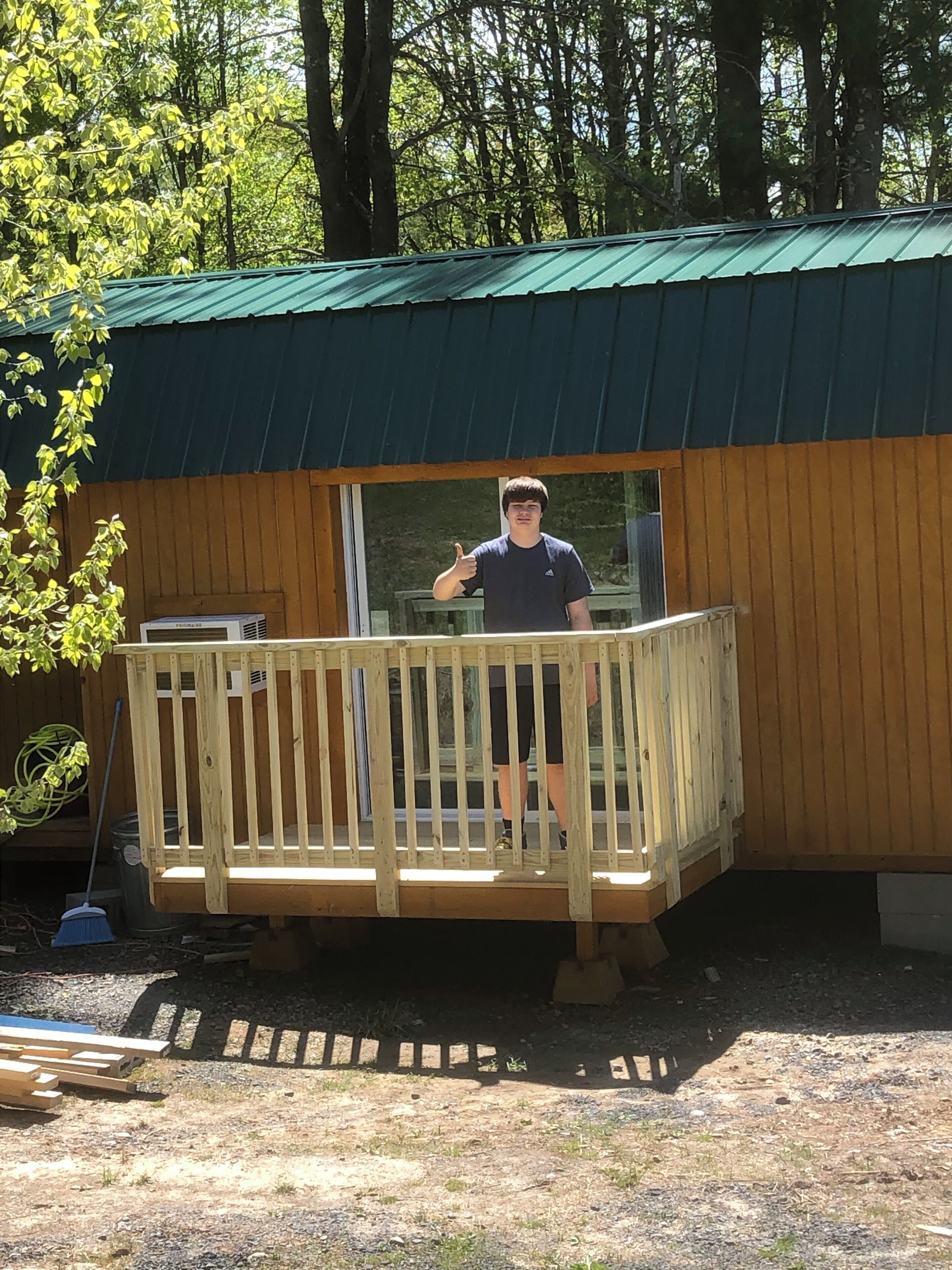 Une terrasse en bois attenante à un bâtiment doté d’un toit végétalisé, entourée d’arbres.