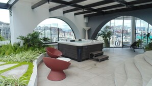 Um terraço moderno no telhado com hidromassagem, área de estar e vista para a cidade.
