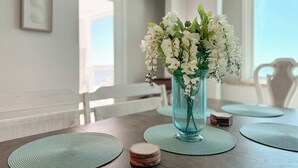 A dining table with a vase of white flowers, placemats, and coasters. - Beachfront Bliss! Spacious 1,800 Sq ft 3BR Sleeps 12 - Oceans 9D - Gulfshores  (Gulf Shores)
