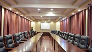 A conference room with a long table and chairs, a projector screen, and curtains on the walls. - Youyichun Business Hotel (Zhao County)