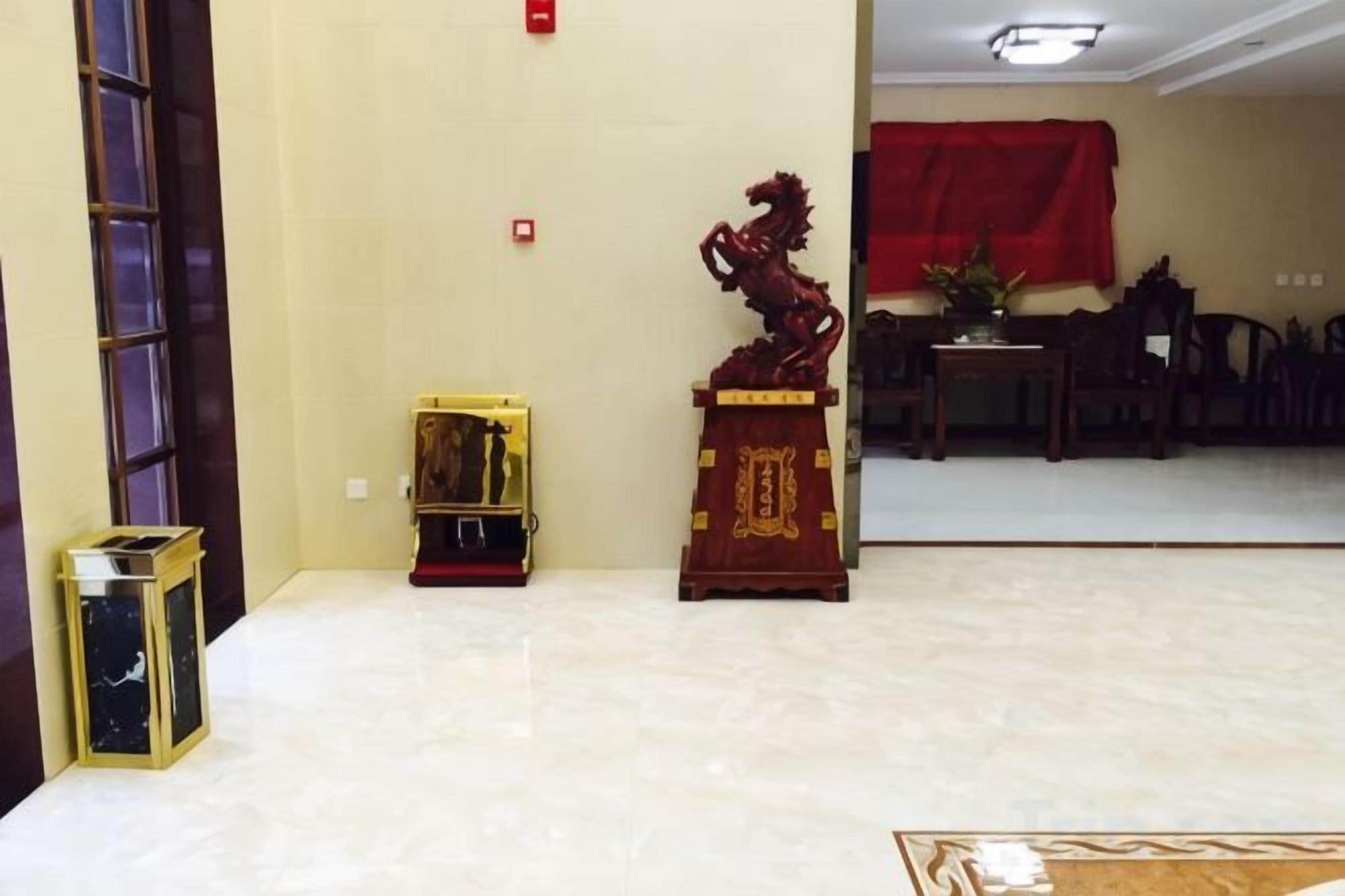A room with a tiled floor, a red decorative item on a stand, a small table with a plant, and a red cloth on a table in the background.