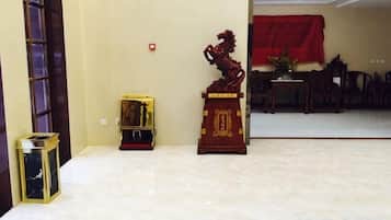A room with a tiled floor, a red decorative item on a stand, a small table with a plant, and a red cloth on a table in the background.