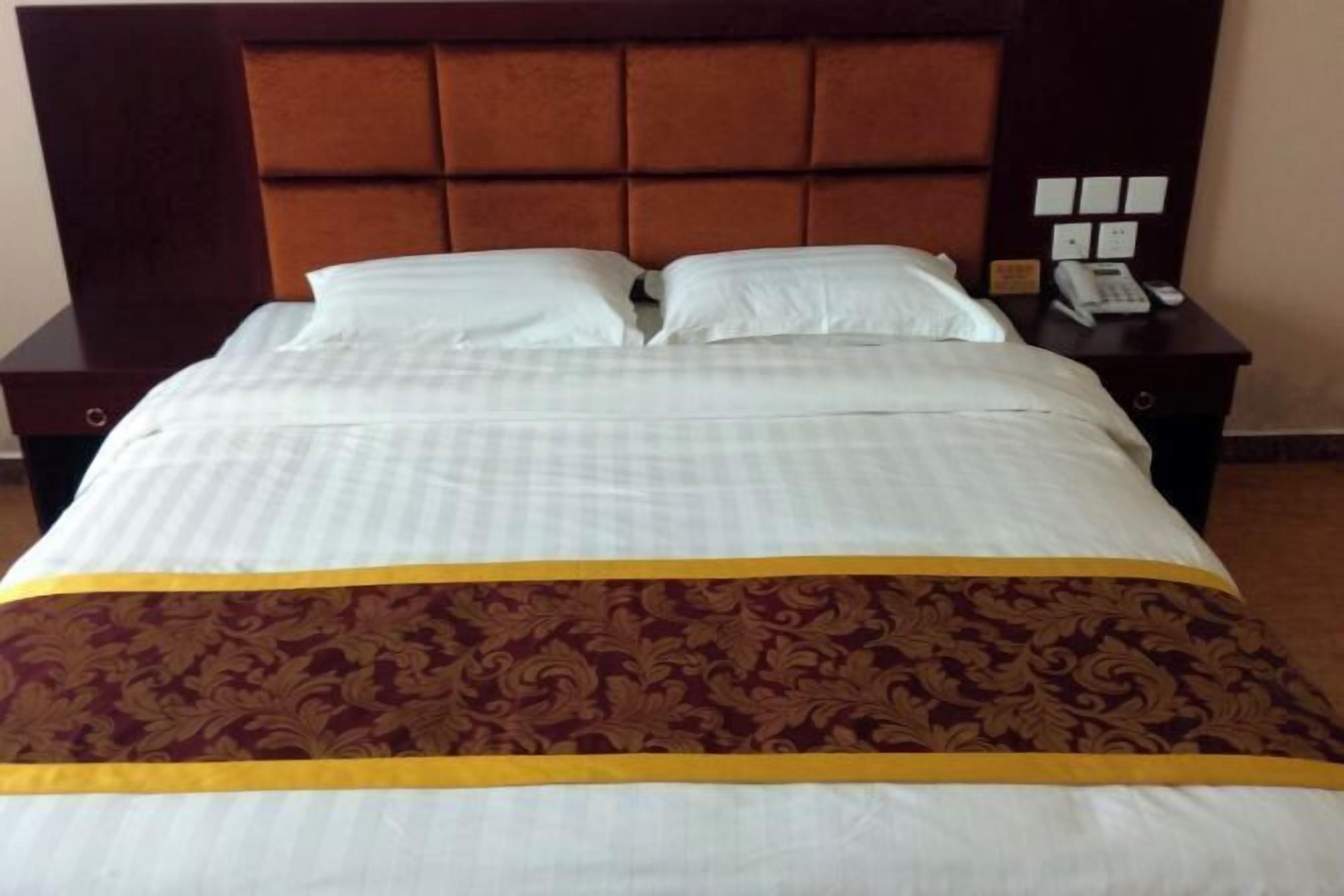 A neatly made bed with a white and maroon bedspread, a wooden headboard, and a nightstand with a telephone.