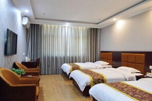 Habitació d'hotel amb tres llits, un televisor, una taula de treball i una cadira.