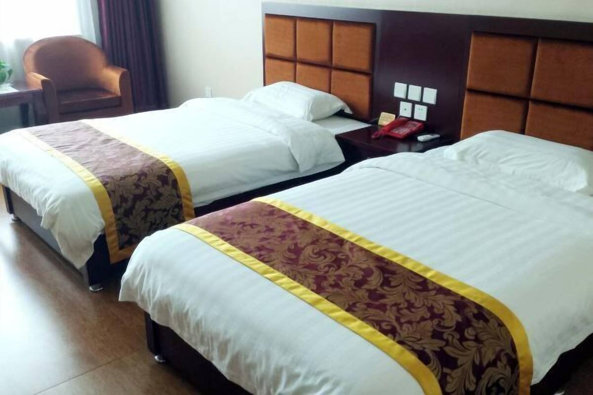 Hotellihuone, jossa on kaksi sänkyä. Jokaisessa sängyssä on valkoinen ja kultainen peitto, puinen pääty ja yöpöytä, jossa on punainen puhelin.