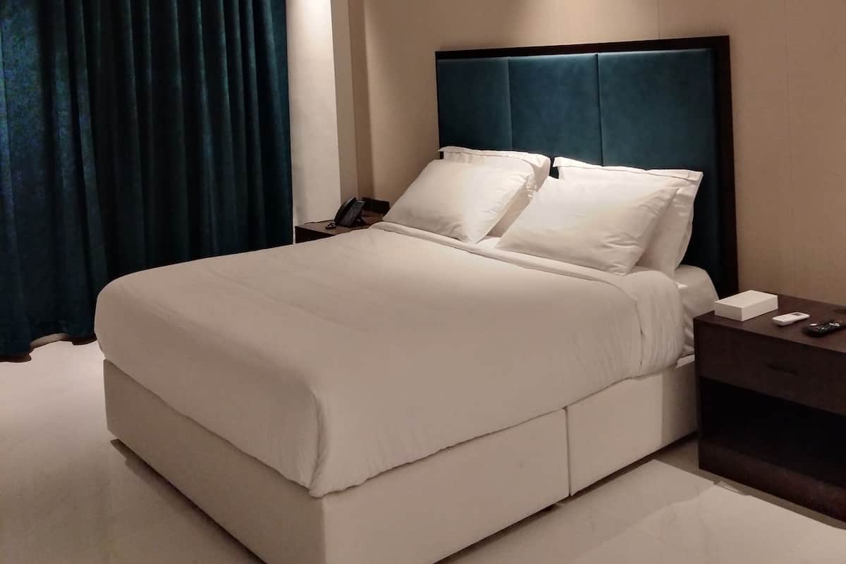 A modern hotel room with a large bed, a dark headboard, and a nightstand with a phone and remote control.