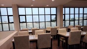 A restaurant with multiple tables and chairs, large windows, and a view of the outside. - Nebula Hotel (Duqm)