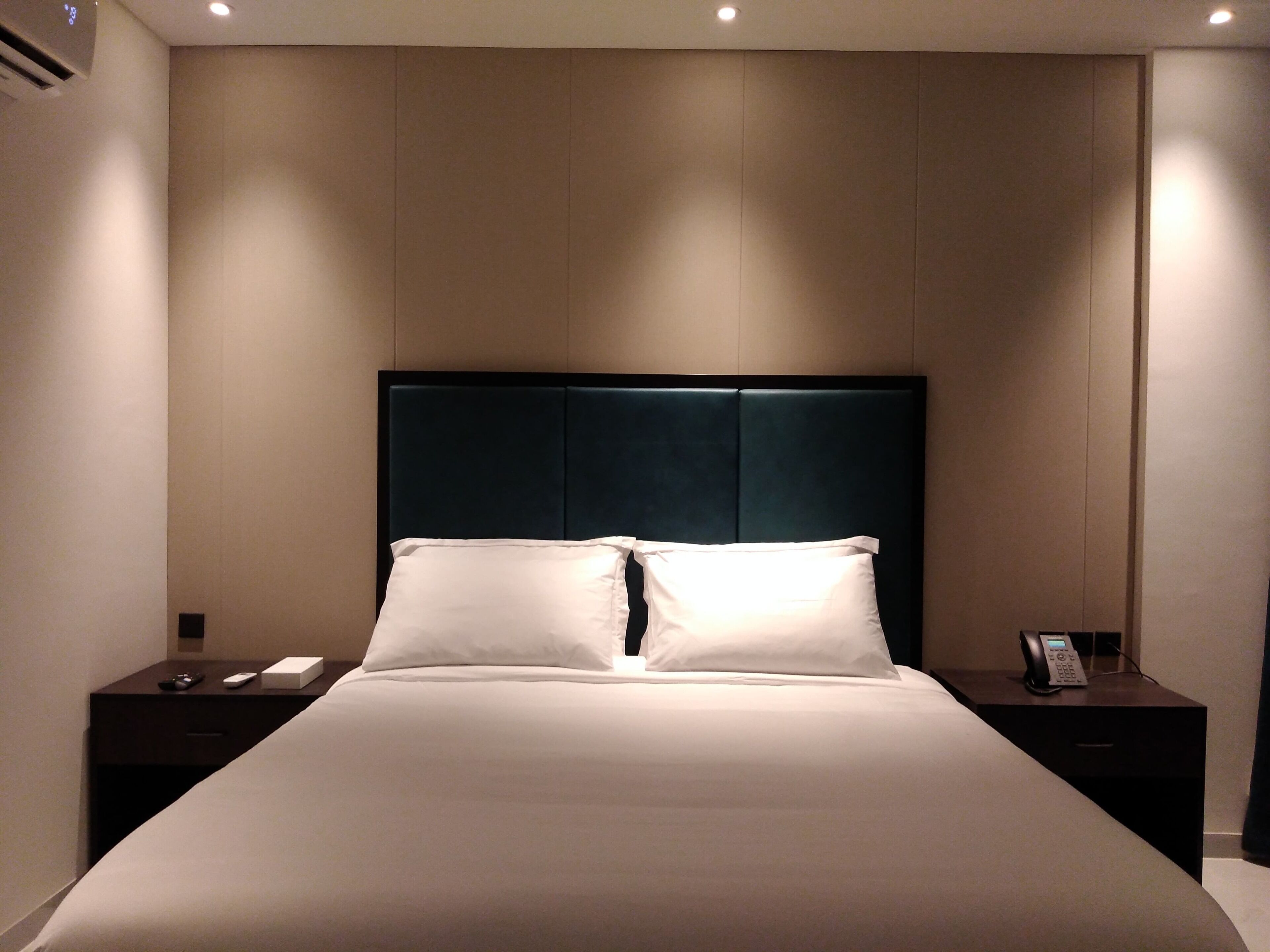 Un lit bien fait, avec une tête de lit sombre, dans une chambre d’hôtel.