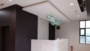 A modern reception area with a marble reception desk, dark wood accents, and a decorative chandelier. - Nebula Hotel (Duqm)