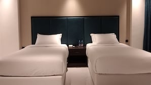 A hotel room with two single beds, a dark headboard, and a nightstand with water bottles. - Nebula Hotel (Duqm)