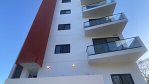 A modern building with a prominent red and white facade, featuring balconies and multiple windows. The name "DellaTerra" is displayed prominently on the front. - Oceanview Penthouse Condo in Sunny Bucerias (Bucerias)